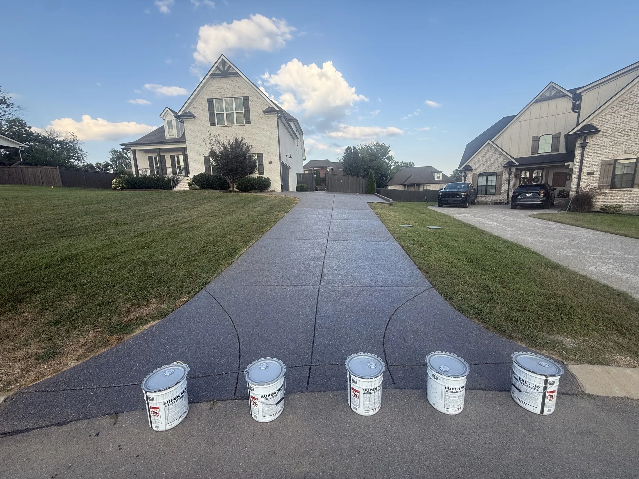 The same driveway after sealing, dark and even, with empty sealer buckets lined up at the street